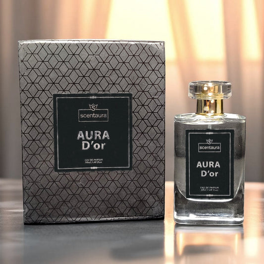 Scentura Aura D'or perfume bottle and packaging on a reflective surface with a blurred background