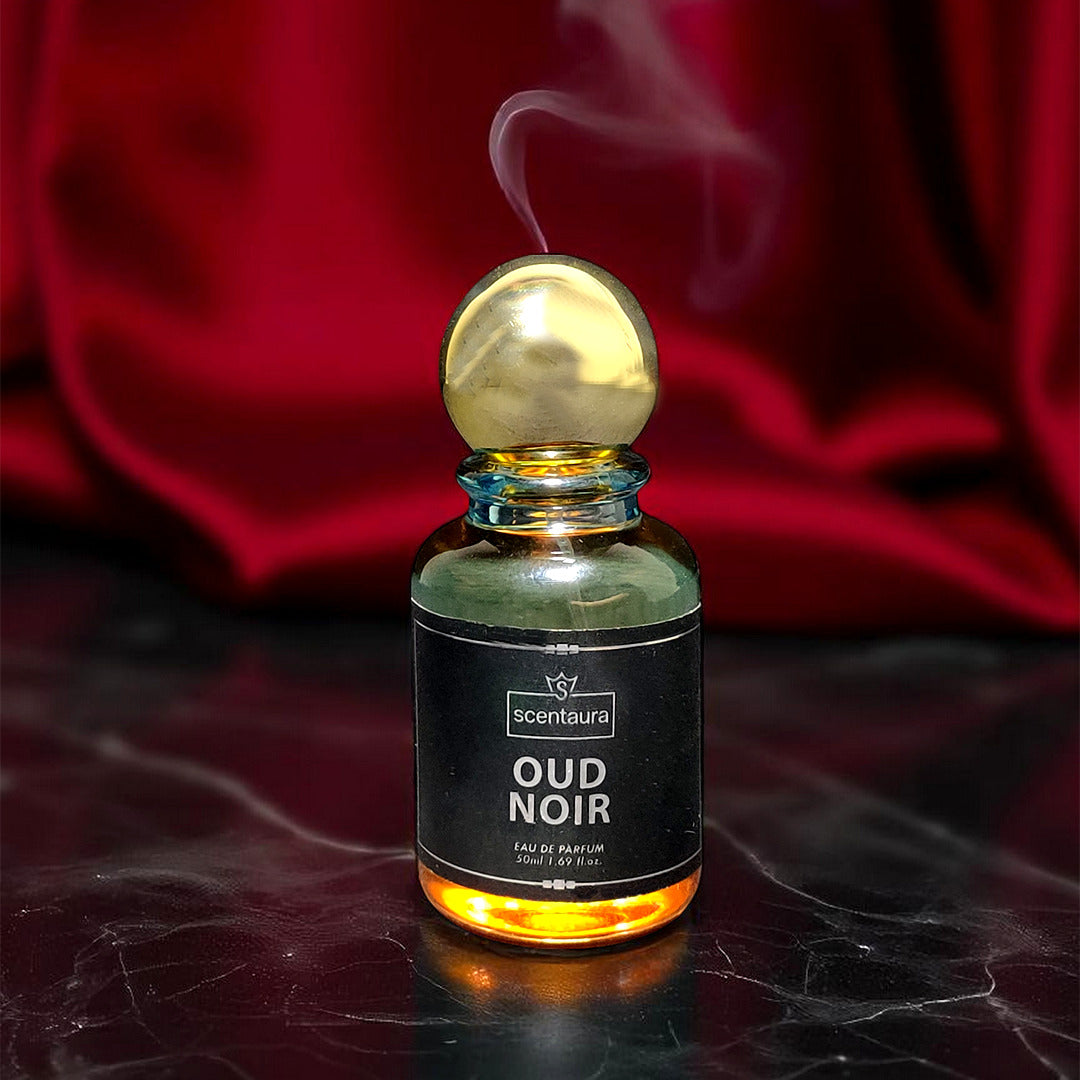 Perfume bottle labeled 'Oud Noir' with a gold cap on a dark surface with red fabric in the background.